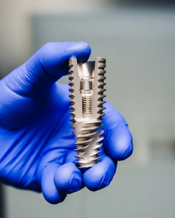 A precision-milled titanium implant component held in a gloved hand